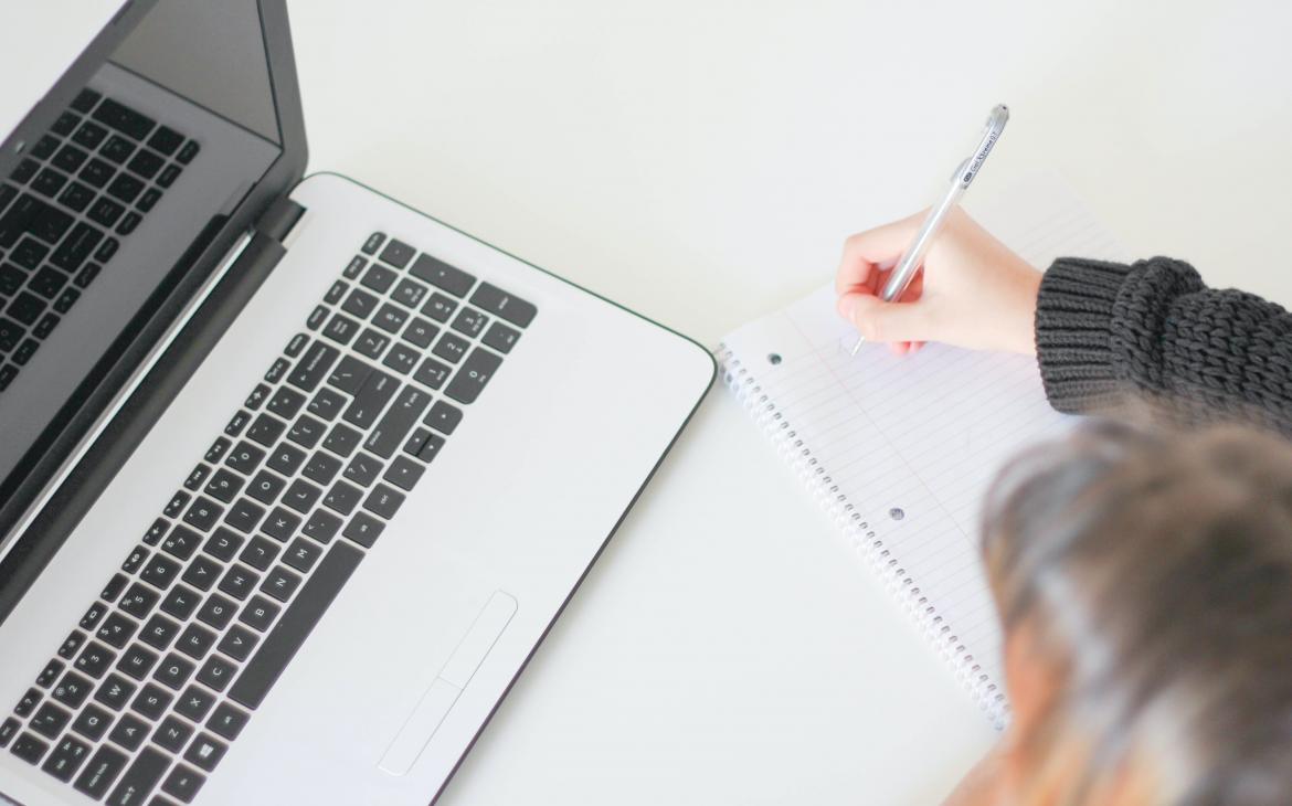 Une personne prend des notes sur un cahier devant son ordinateur